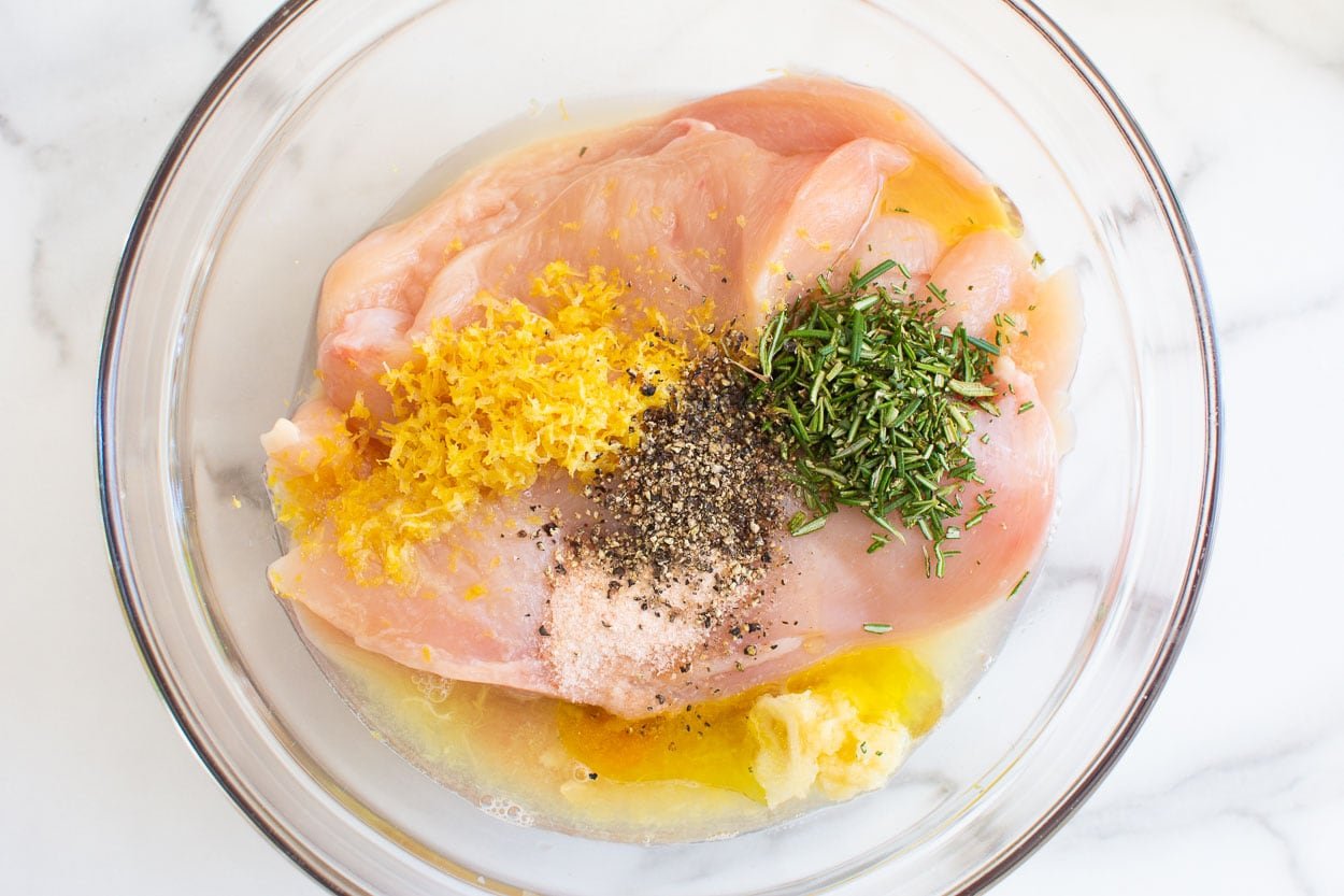 Chicken breasts, lemon zest, rosemary, olive oil, lemon juice, salt and pepper in a bowl.