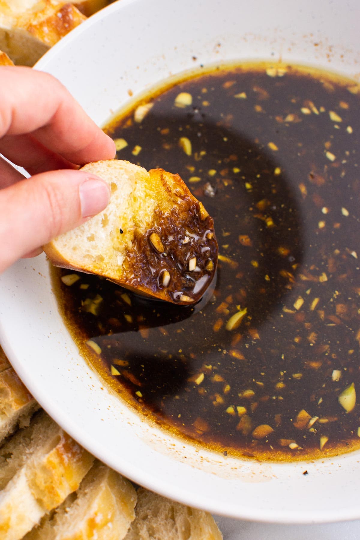 Person dipping a slice of bread in a bowl with olive oil bread dip with garlic.