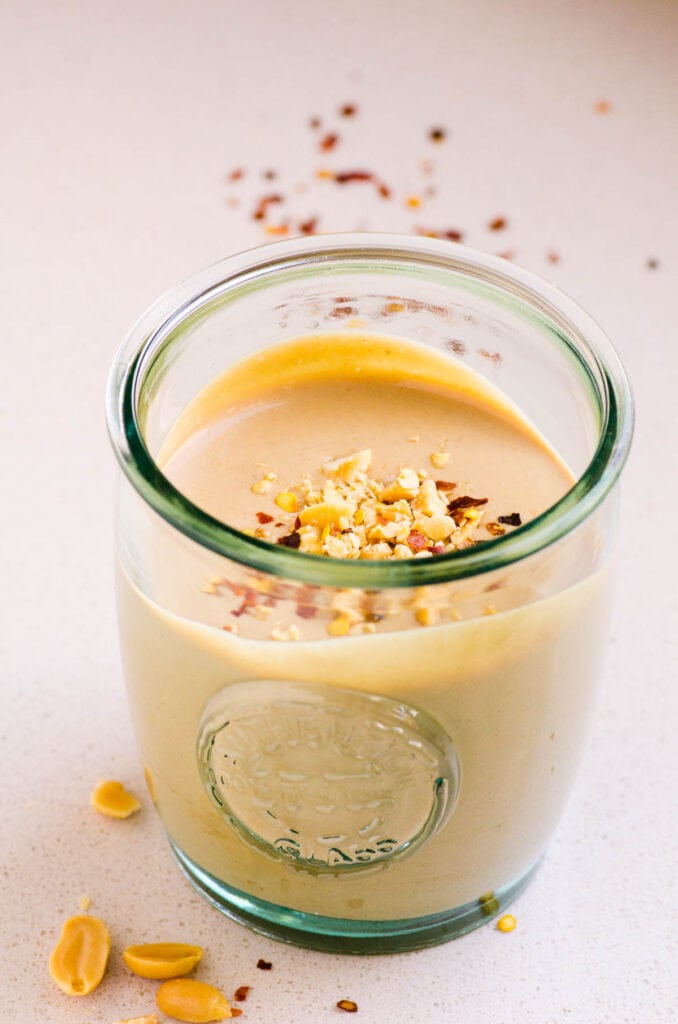 homemade peanut sauce in glass jar with peanuts and chili pepper