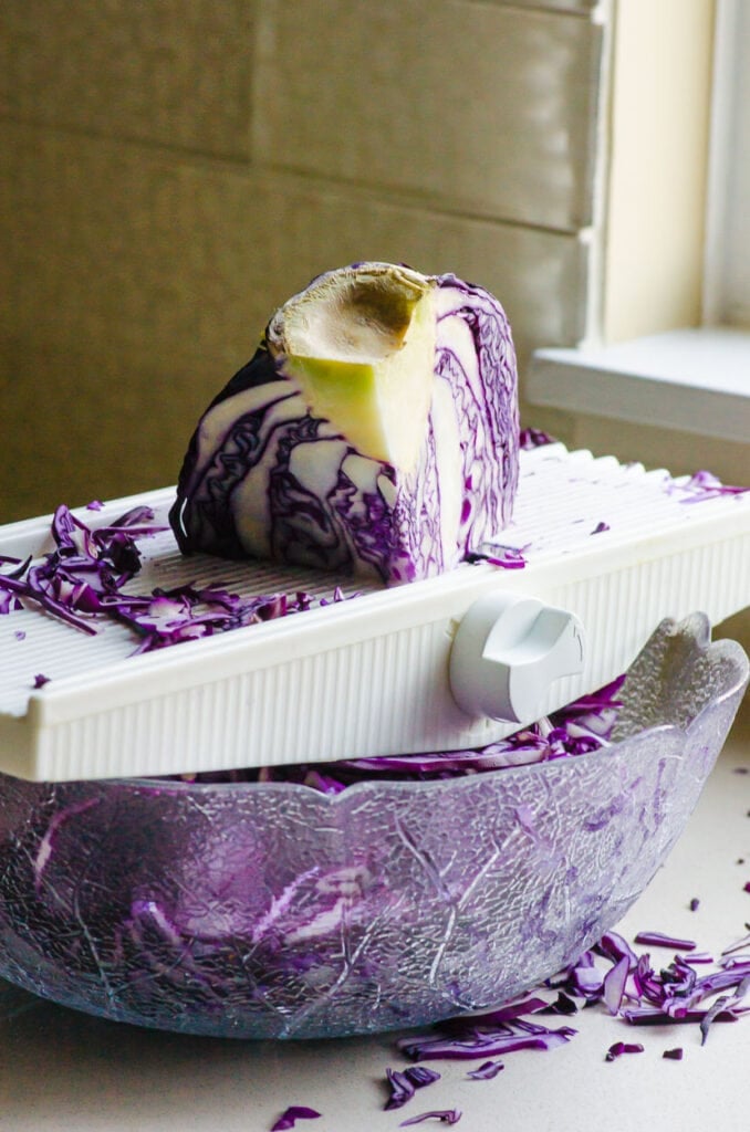 cabbage being shredded on a mandoline into a bowl