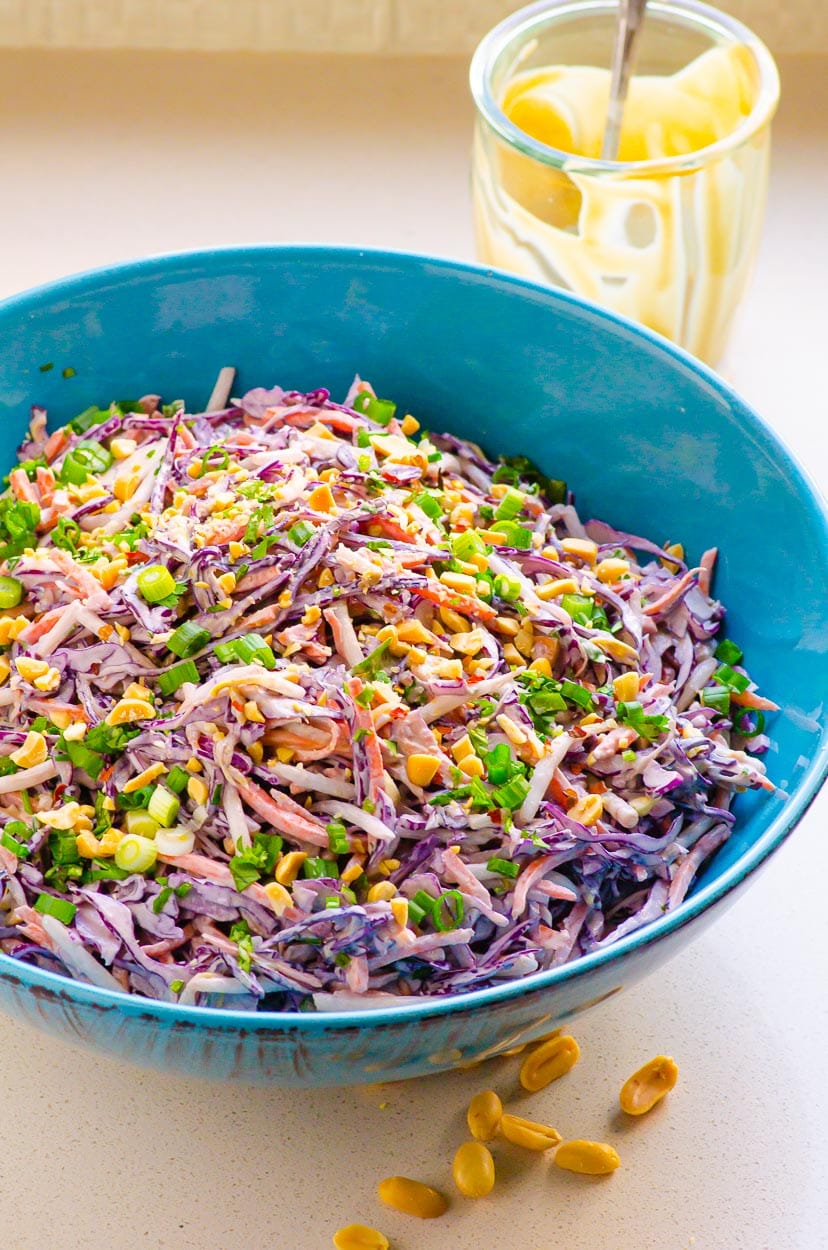 Peanut slaw garnished with peanuts and scallions and empty jar in the background.