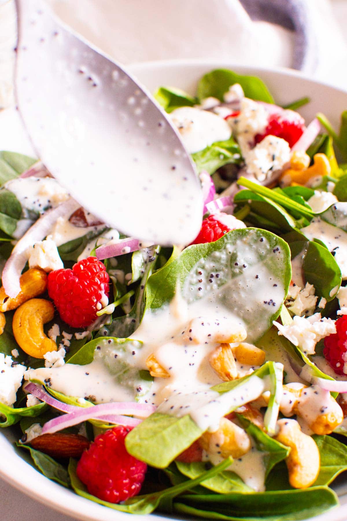 Salad with poppy seed dressing dripping off of spoon into salad.