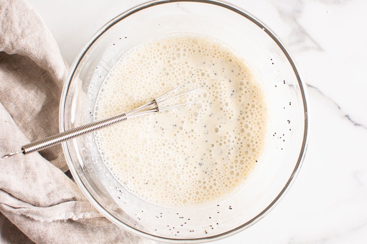 Whisked poppy seed dressing in a glass bowl with a whisk.