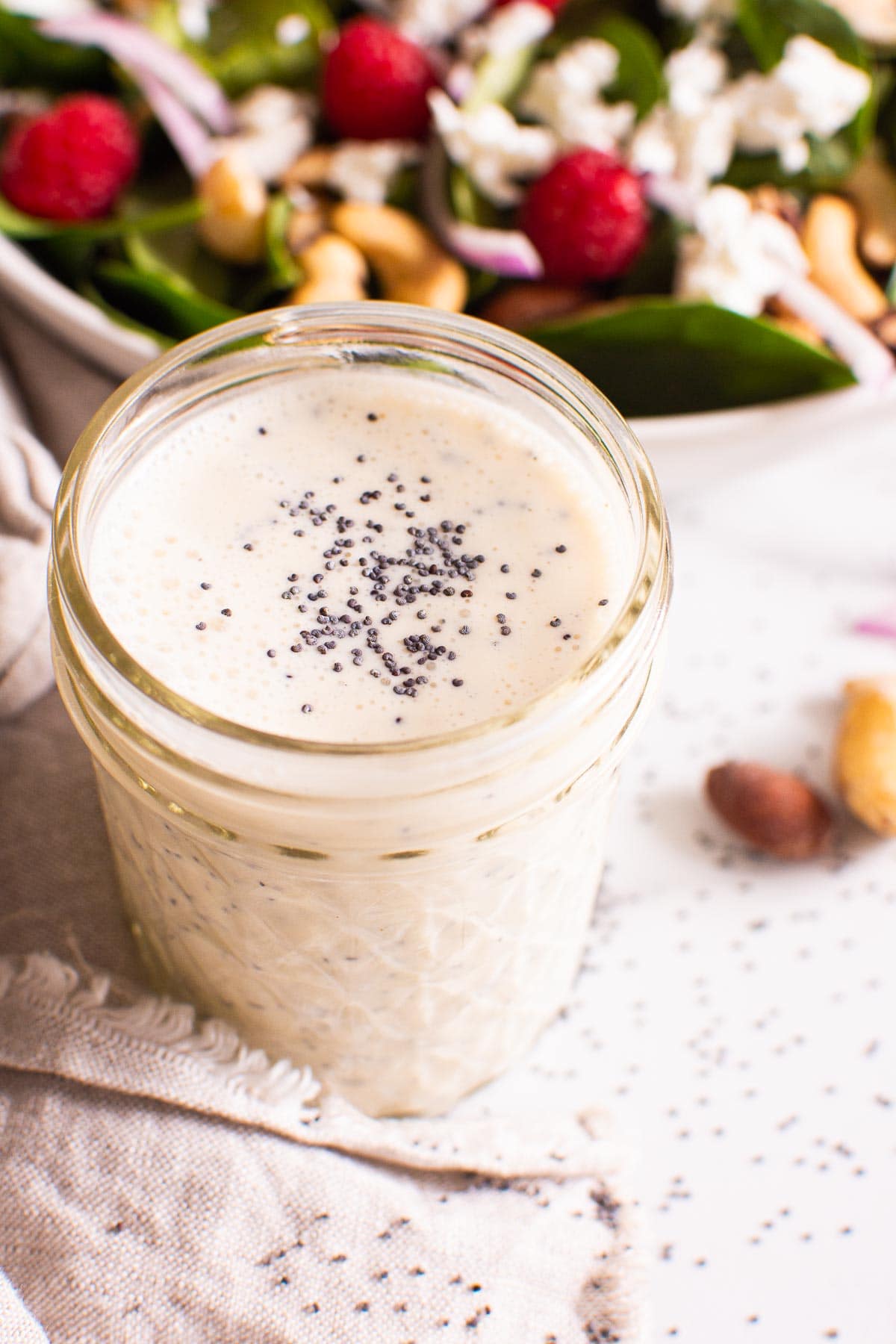 Poppyseed dressing in a glass jar with salad in a bowl in the background.