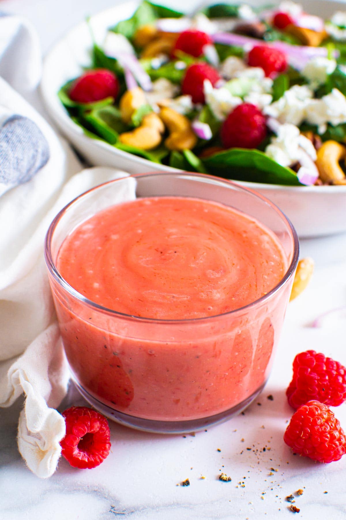 Raspberry vinaigrette dressing in a bowl with salad in the background.