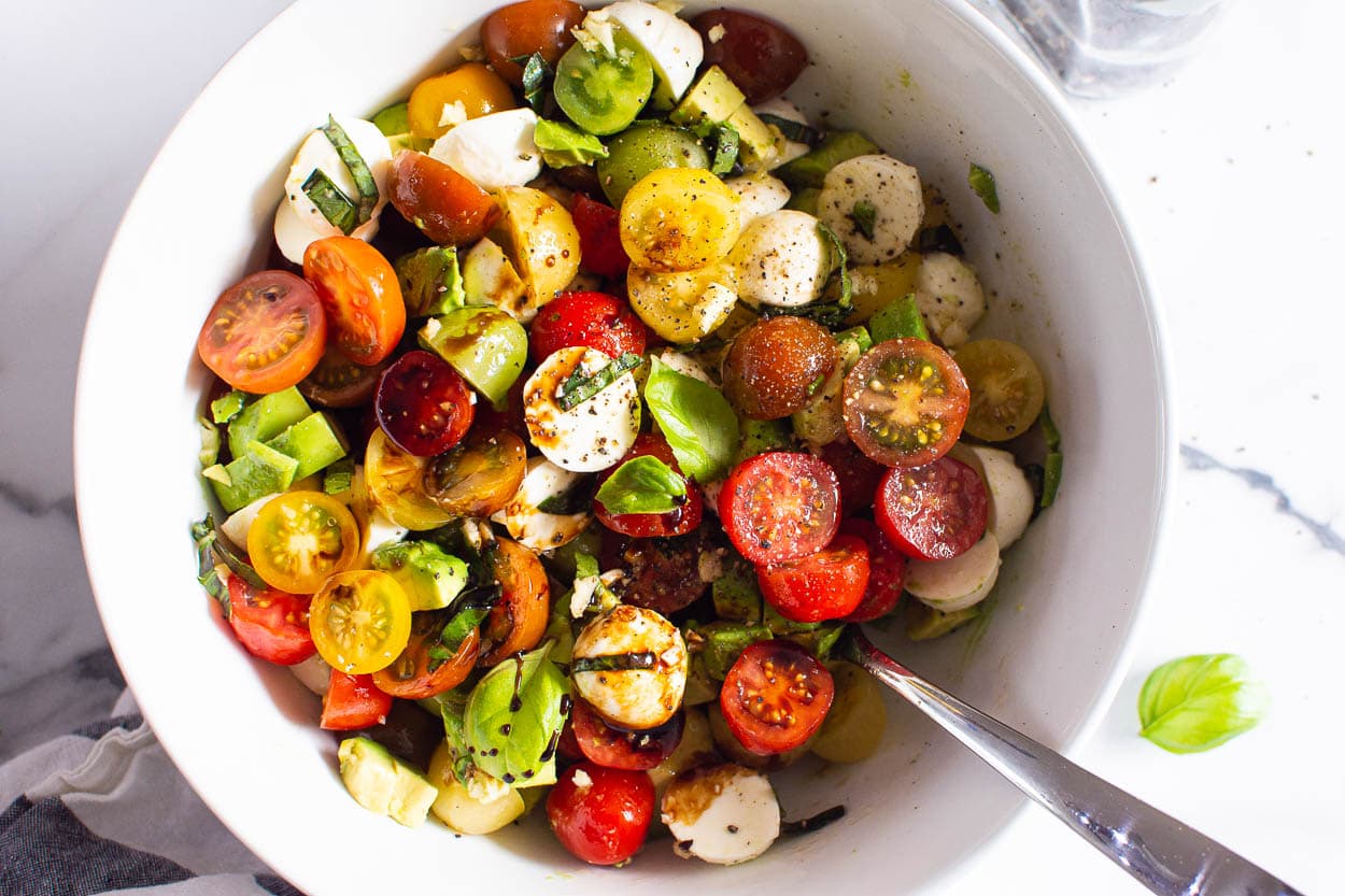 Salad in white bowl with metal spoon.