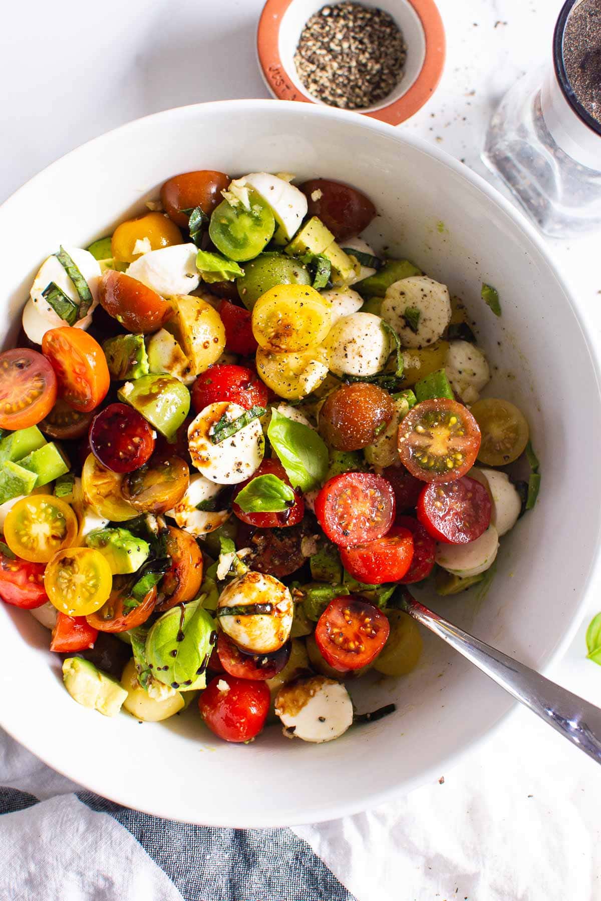 Tomato mozzarella avocado salad in bowl with serving spoon.