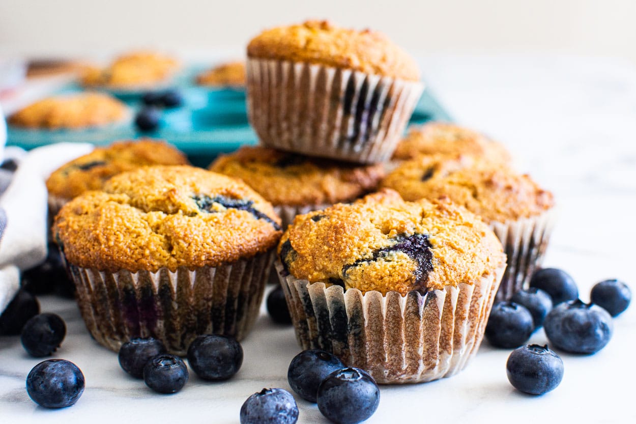 Almond flour blueberry muffins with fresh blueberries and blue muffin tin.