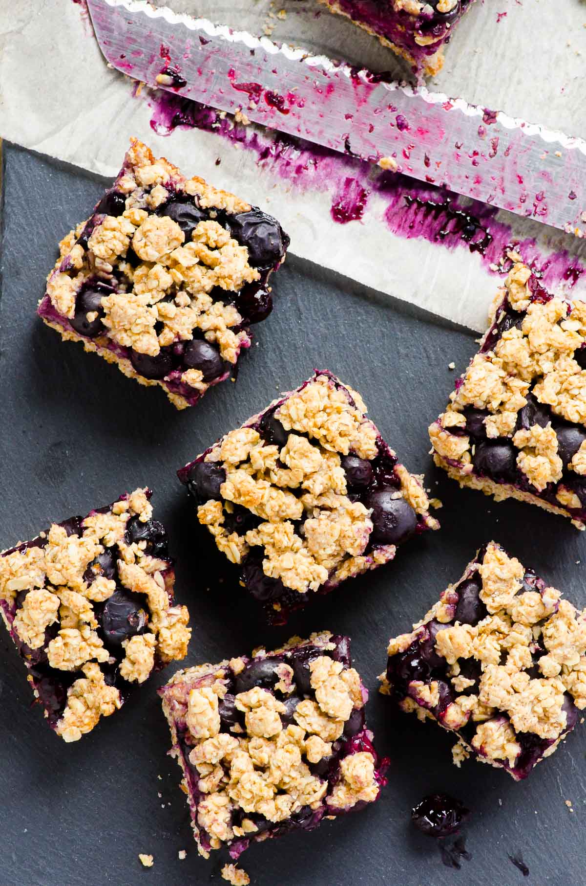 Iced blueberry oatmeal bars on black serving dish with a knife on parchment paper.