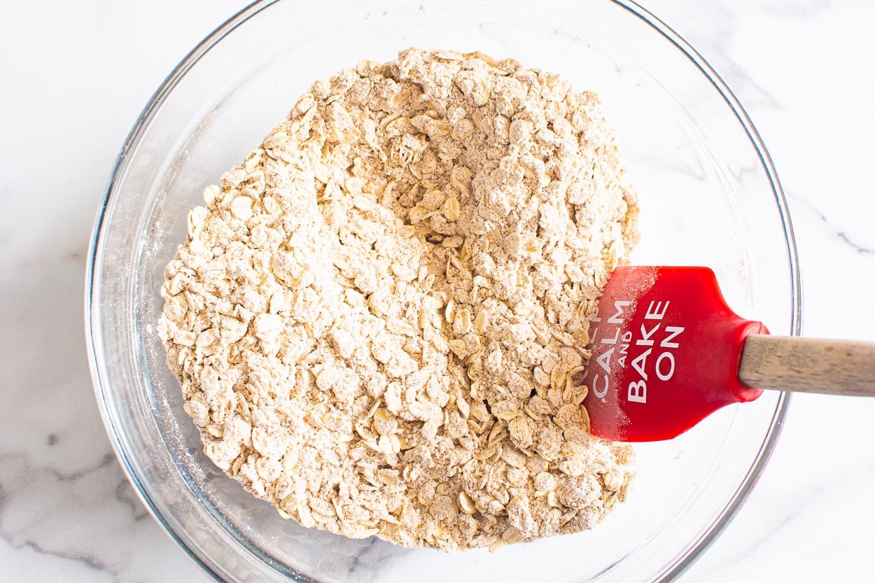 Oats mixed with other dry ingredients in a bowl with spatula.