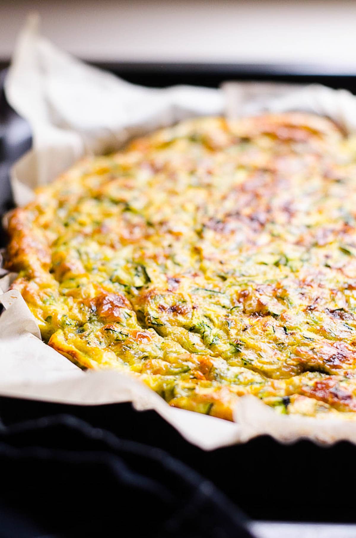 Crustless zucchini quiche in parchment lined pie dish.