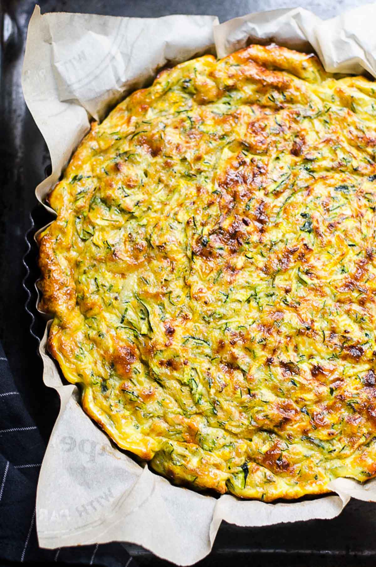 Zucchini quiche in a tart pan lined with parchment paper.