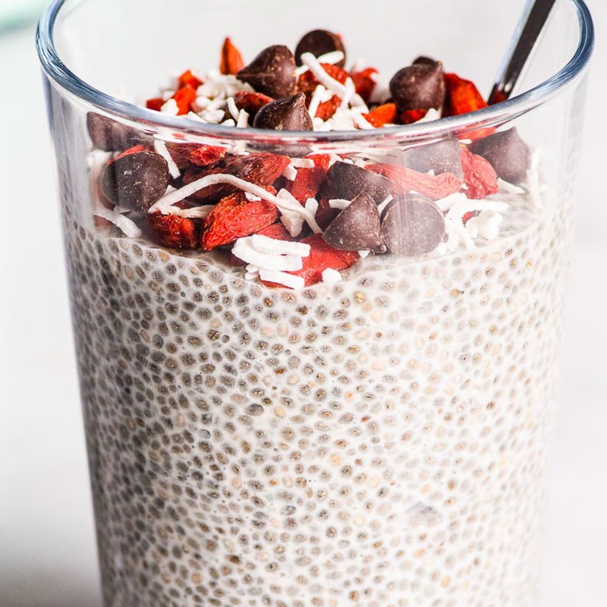 Overnight chia pudding in a glass with dried berries, chocolate chips and coconut flakes.