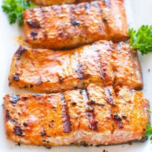 Three grilled salmon fillets with parsley on a plate.