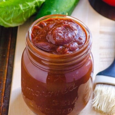 healthy bbq sauce in a jar with a basting brush and greens to the side of jar