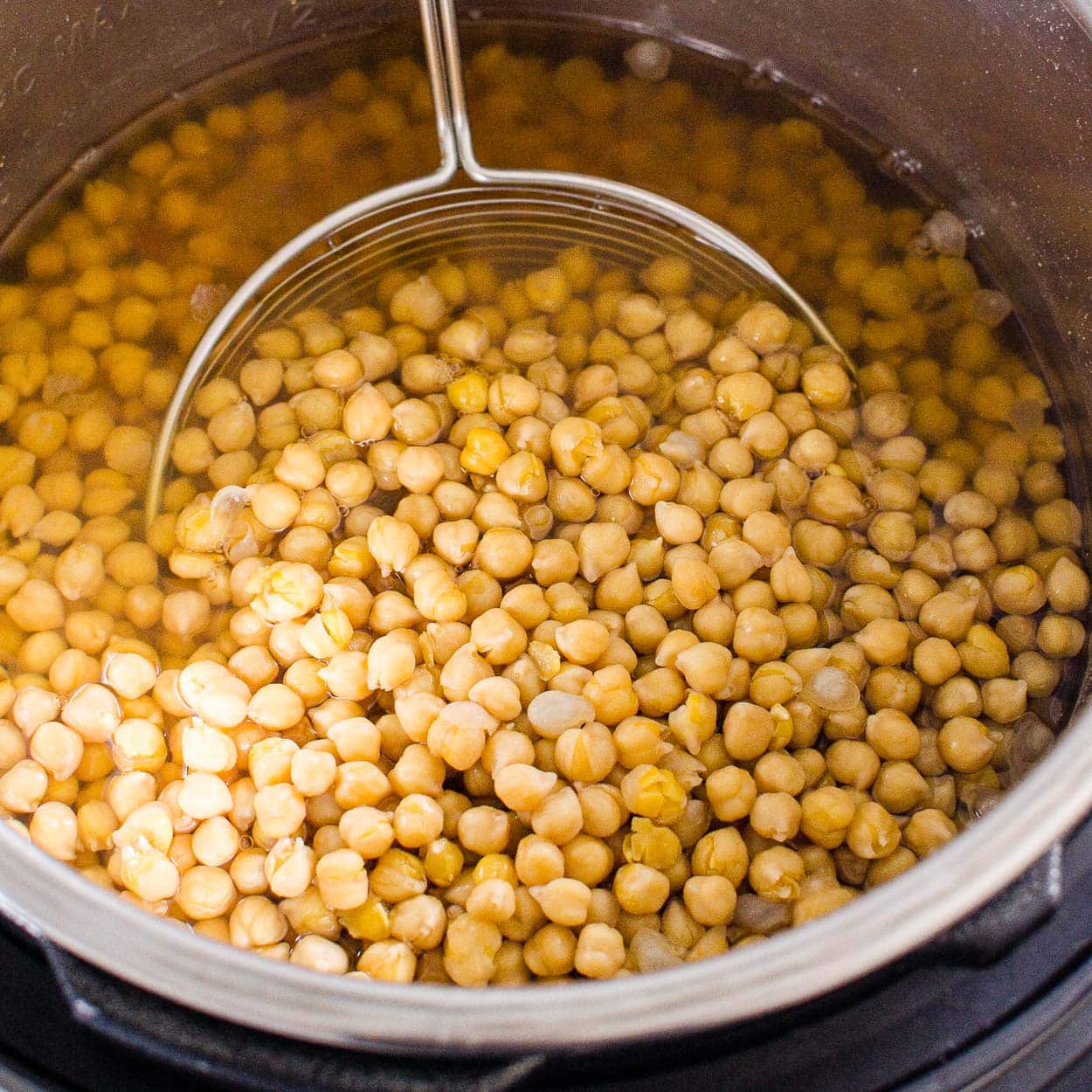 Cooked Instant Pot chickpeas with a strainer inside pressure cooker pot.