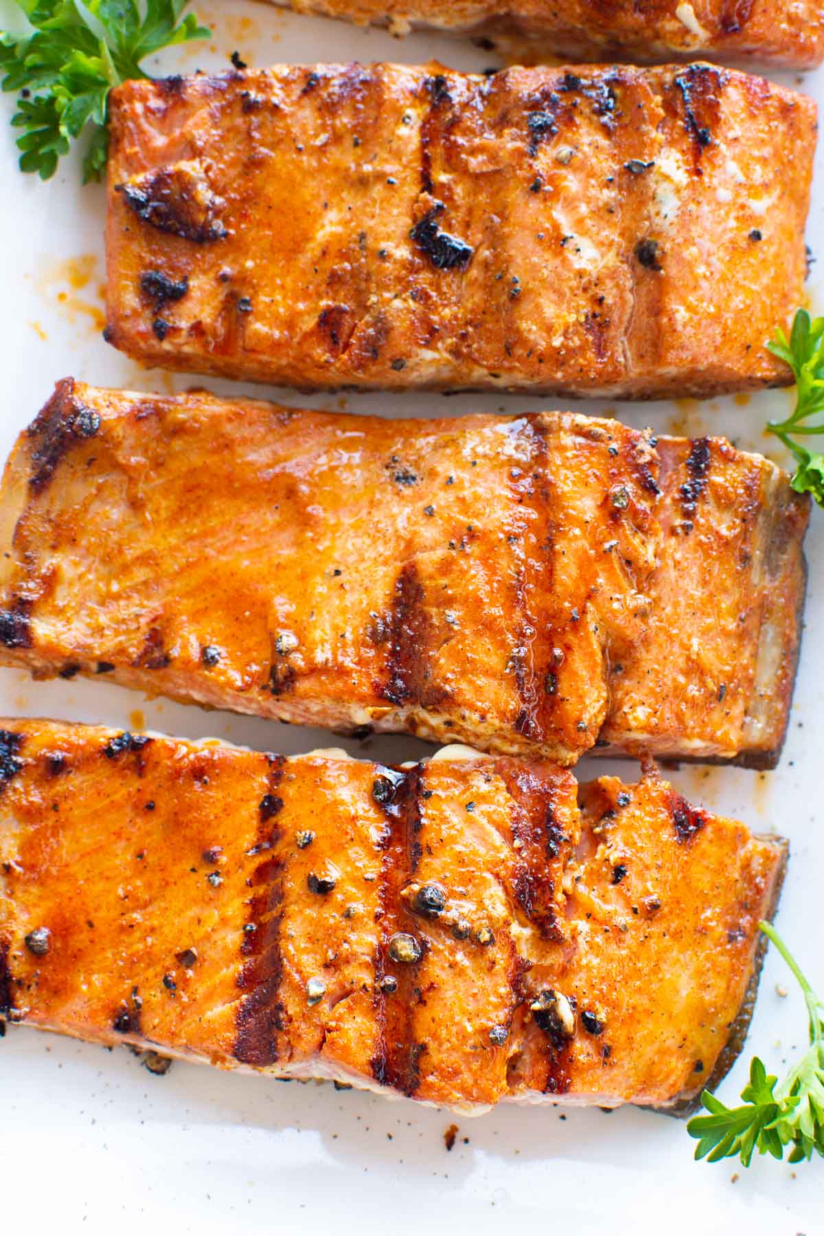 Three grilled salmon fillets on white plate with parsley garnish.