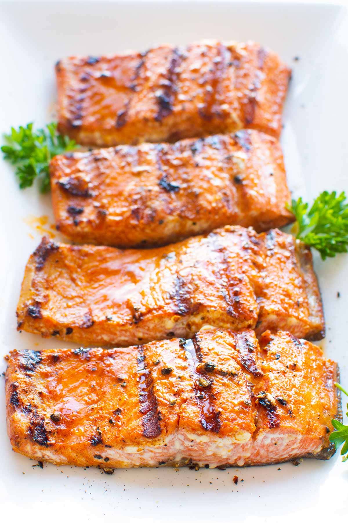 Grilled salmon slices on white plate with parsley.