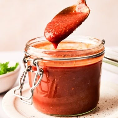 Healthy BBQ sauce dripping from a spoon into a glass jar.