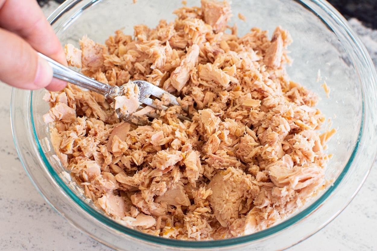 Flaking canned tuna with a fork in a bowl.