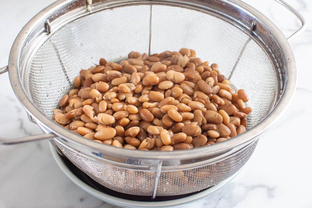 Cooked pinto beans in a colander placed on a plate.