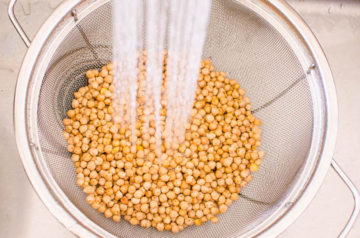 Rinsing dried chickpeas in a colander in sink.
