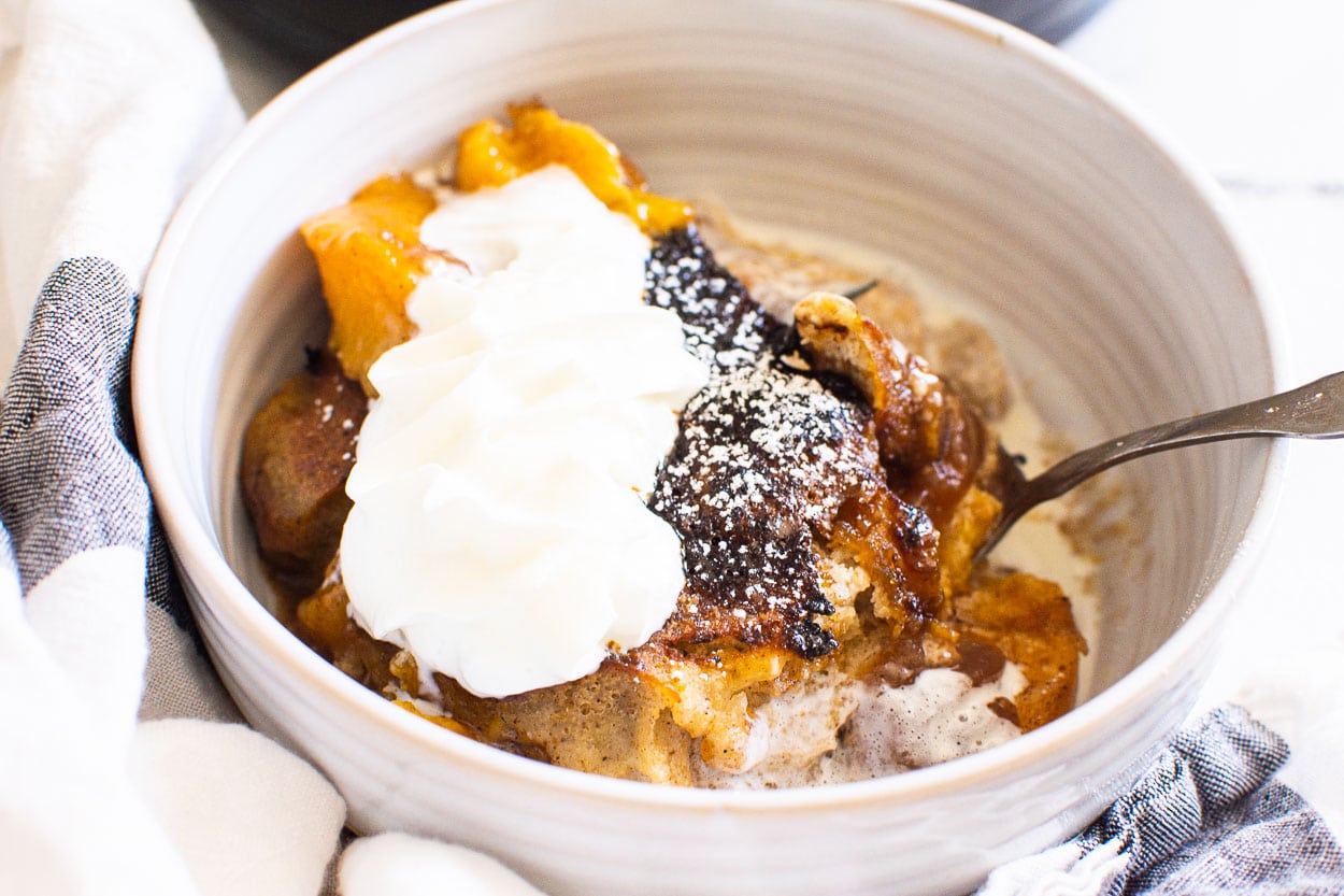 Instant pot peach cobbler in white bowl served with whipped cream.