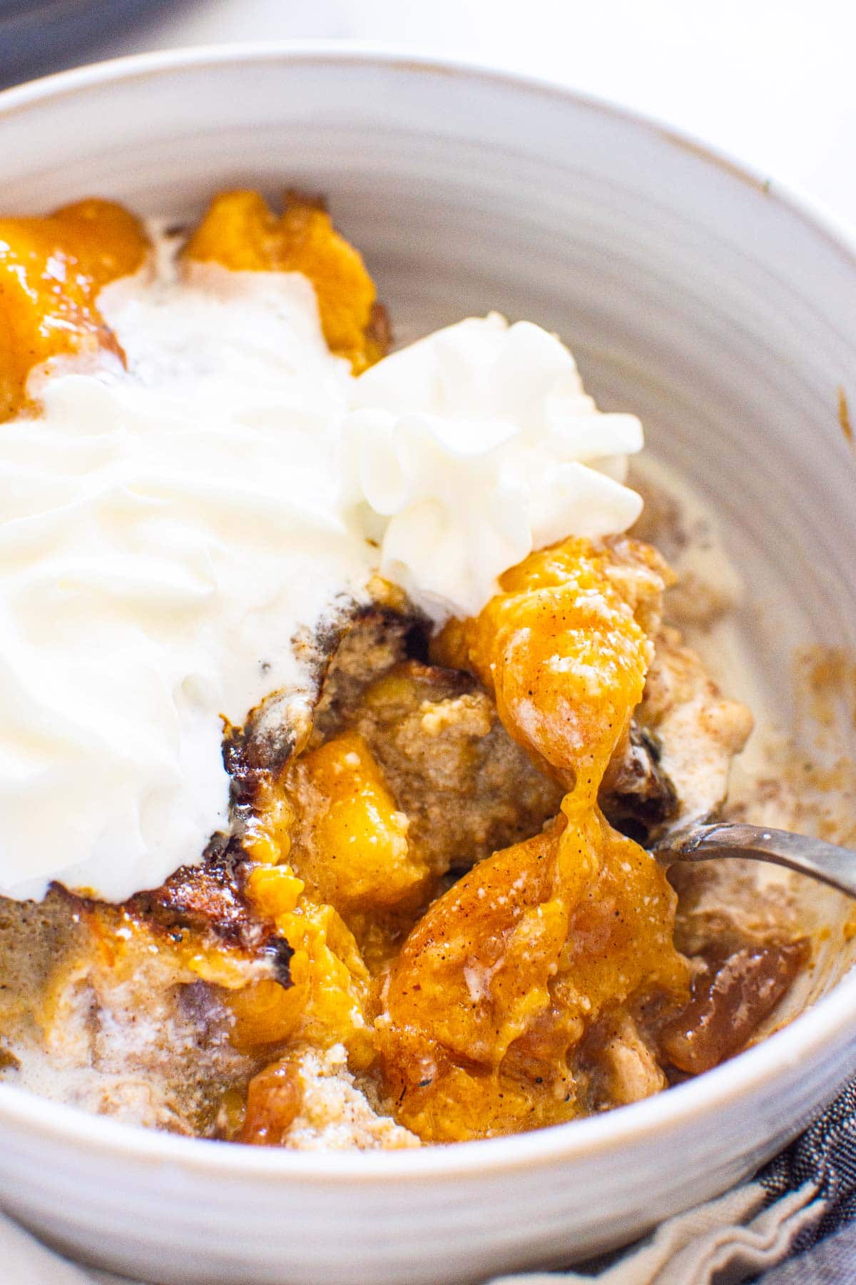Instant pot peach cobbler in bowl with spoon and whipped cream.