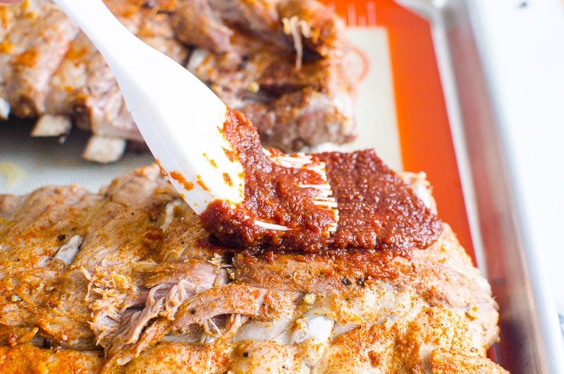 Person brushing cooked Instant Pot ribs with homemade BBQ sauce.