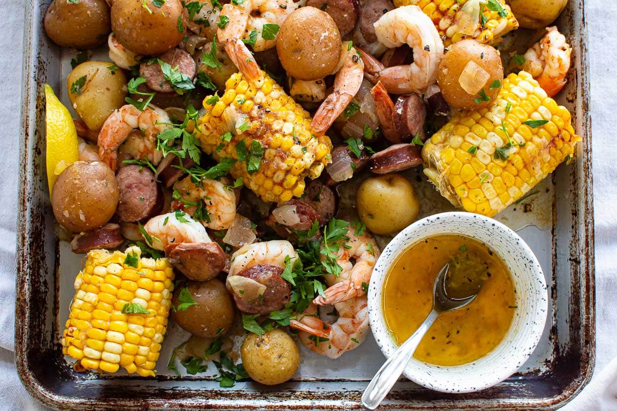 Shrimp boil with potatoes, sausage and corn on serving pan with butter in bowl.