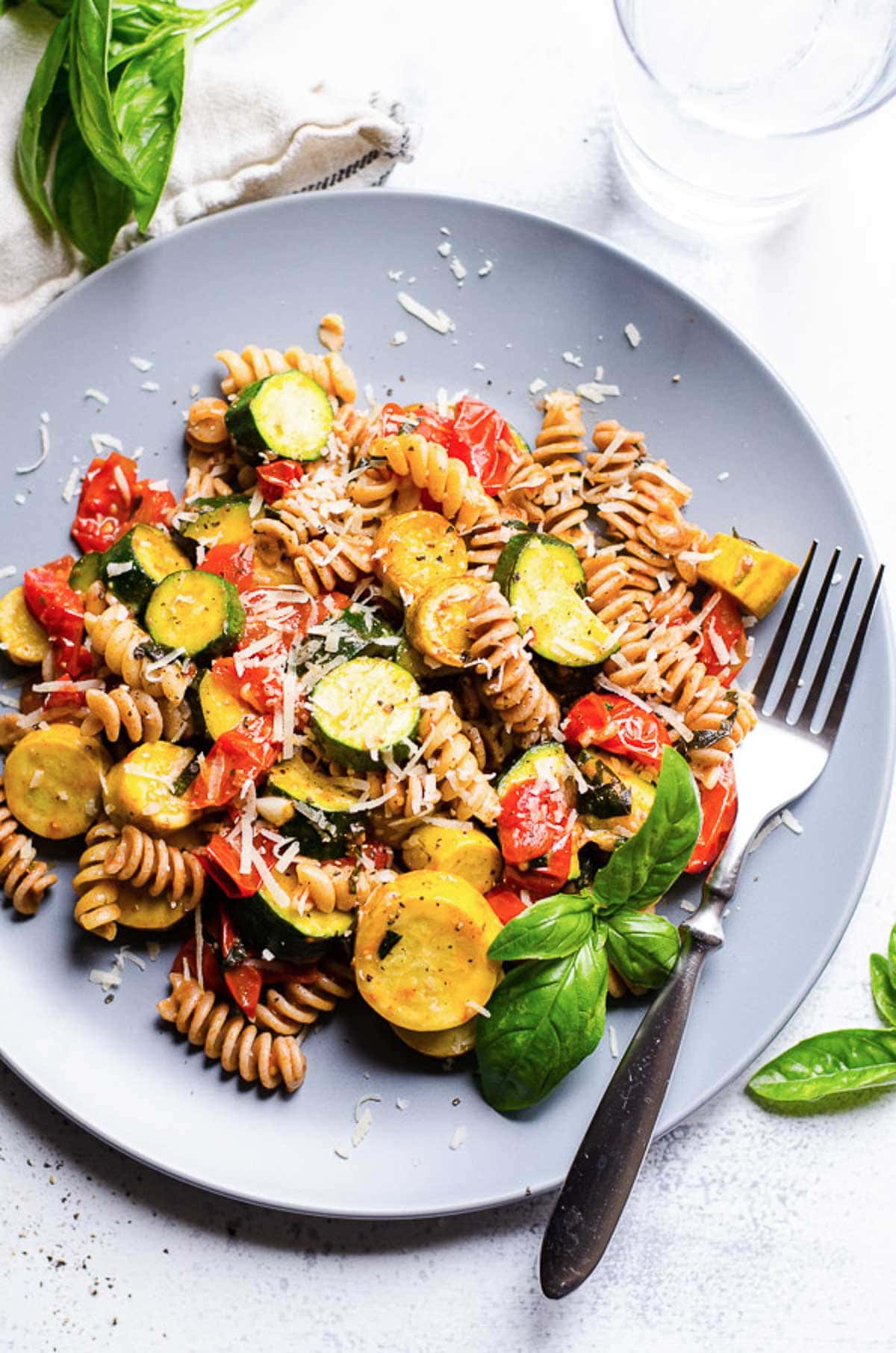 Pasta with zucchini and tomatoes served on a blue plate with a fork.