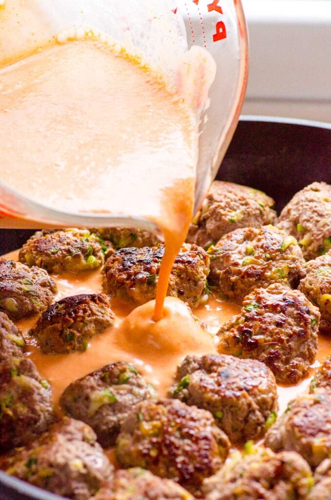 Sauce poured on pan fried meatballs in a skillet.