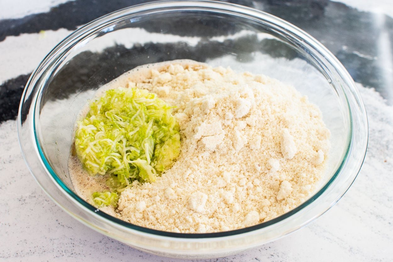 Zucchini and almond flour in a bowl with liquid ingredients.