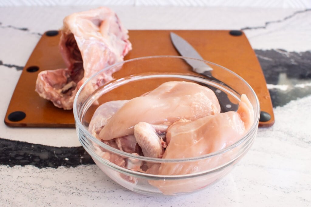 chicken in bowl after cutting with board behind it with carcass of chicken