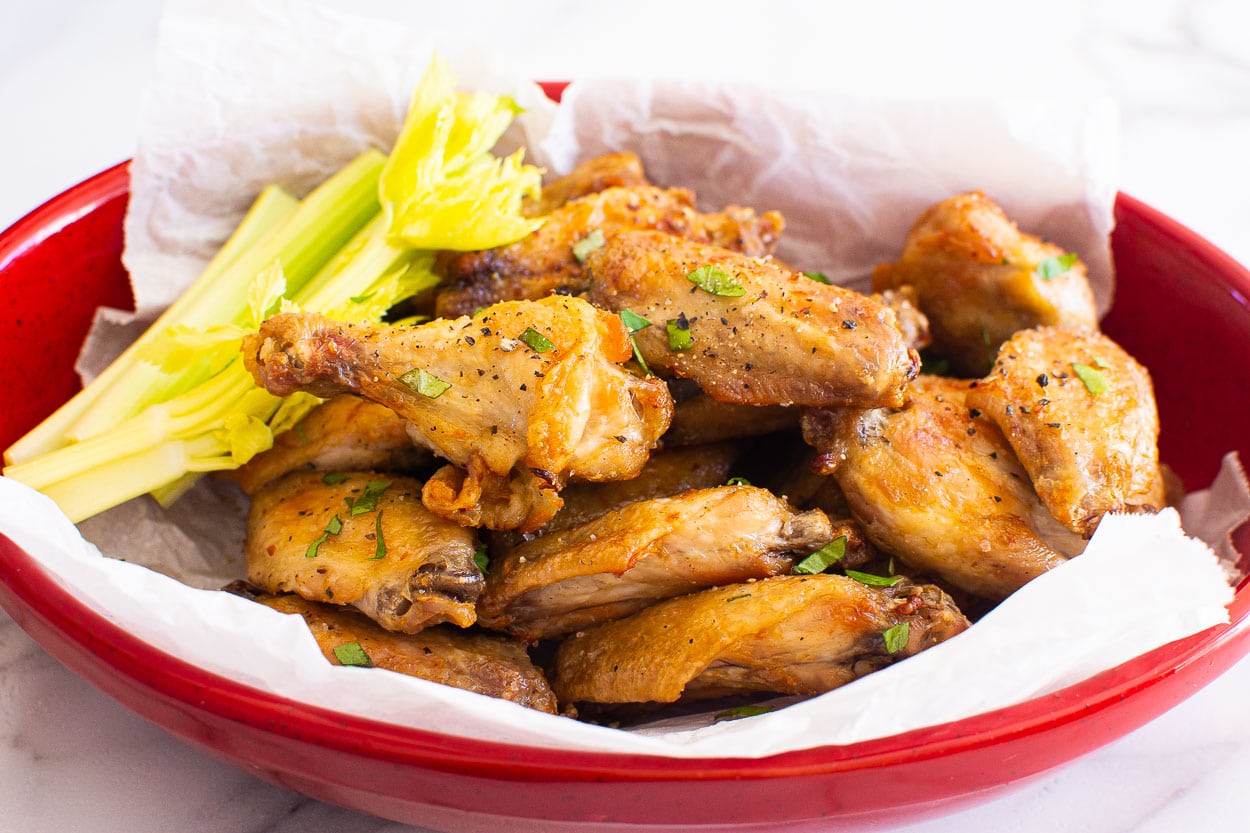 Air fryer salt and pepper chicken wings in red dish with celery sticks.