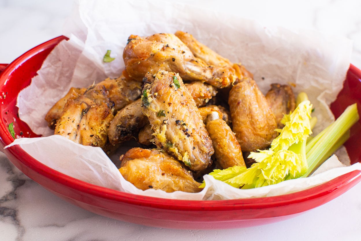 Air fryer lemon pepper chicken wings in red dish with celery sticks.