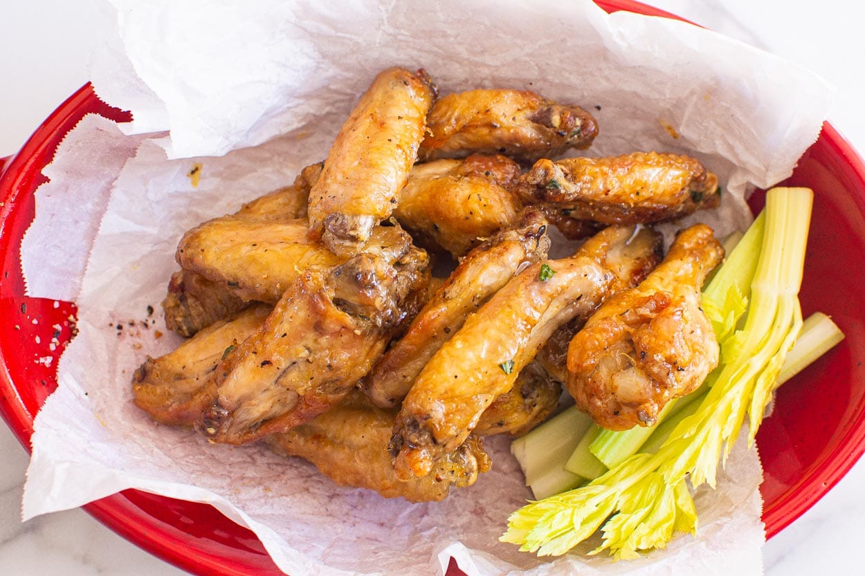 Honey garlic chicken wings in red dish with celery.