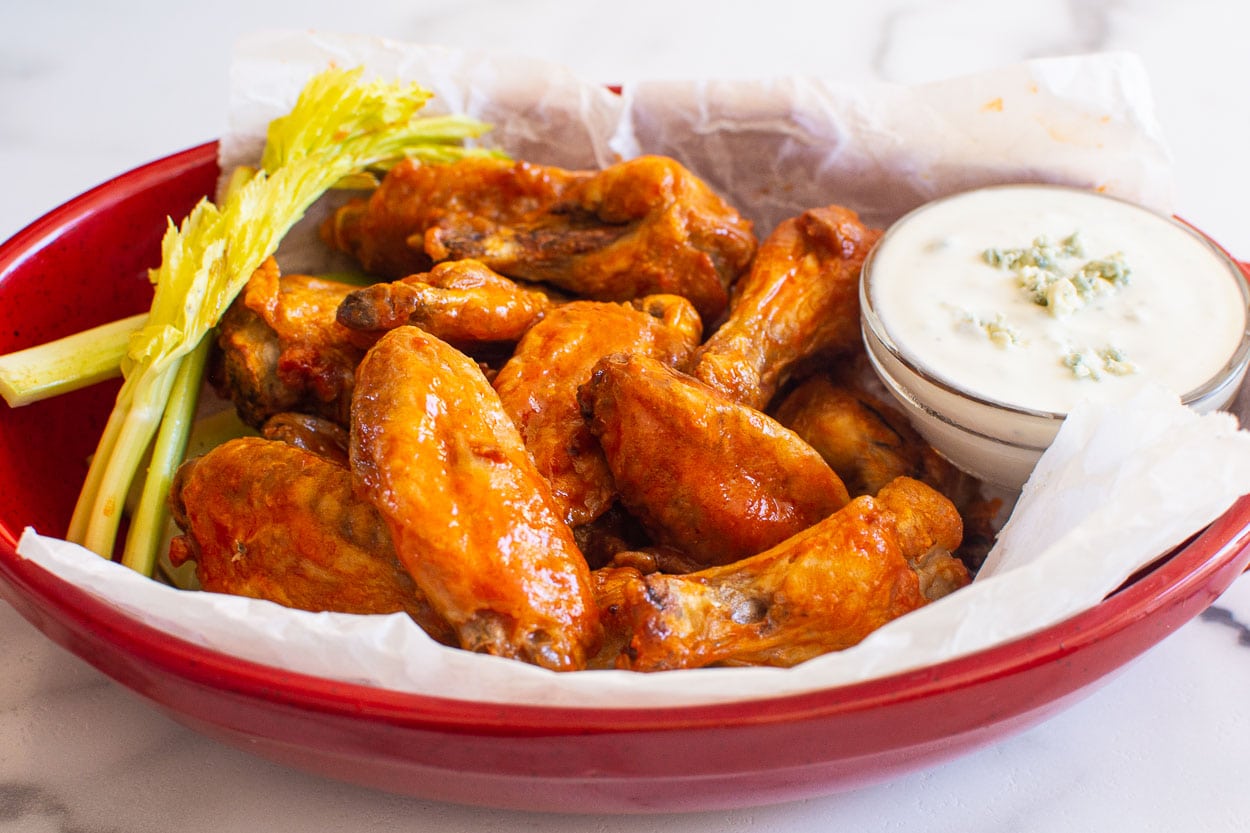 Air fryer buffalo chicken wings in red serving dish with blue cheese sauce and celery.