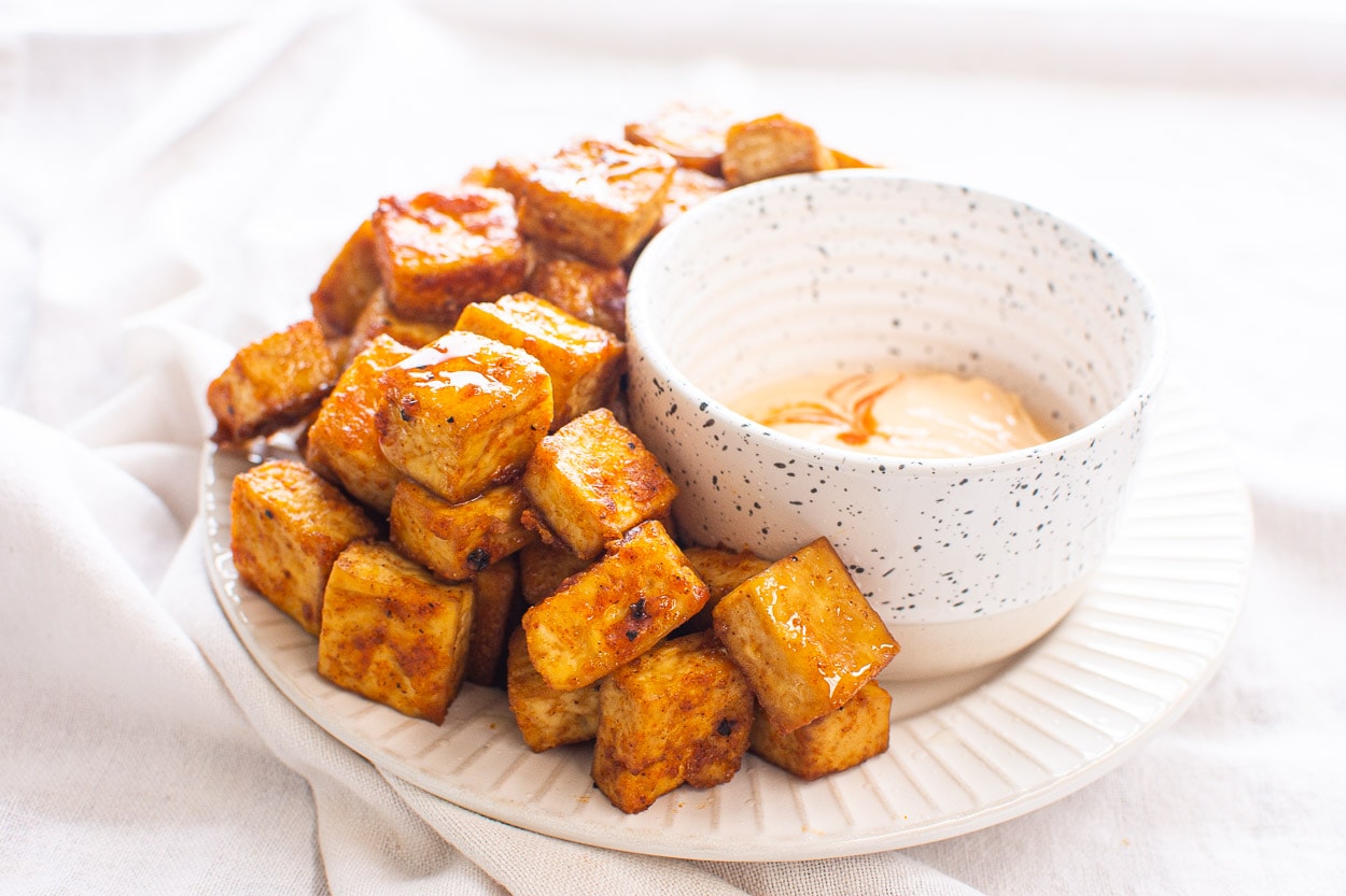 Air fryer tofu on plate with sauce on side in a bowl.