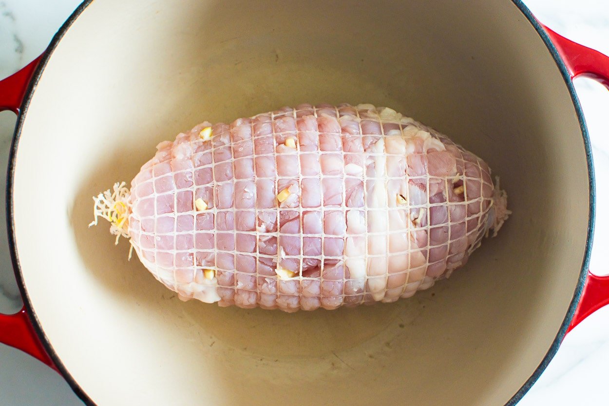 A turkey breast in mesh in a large pot with garlic stuffed into it.