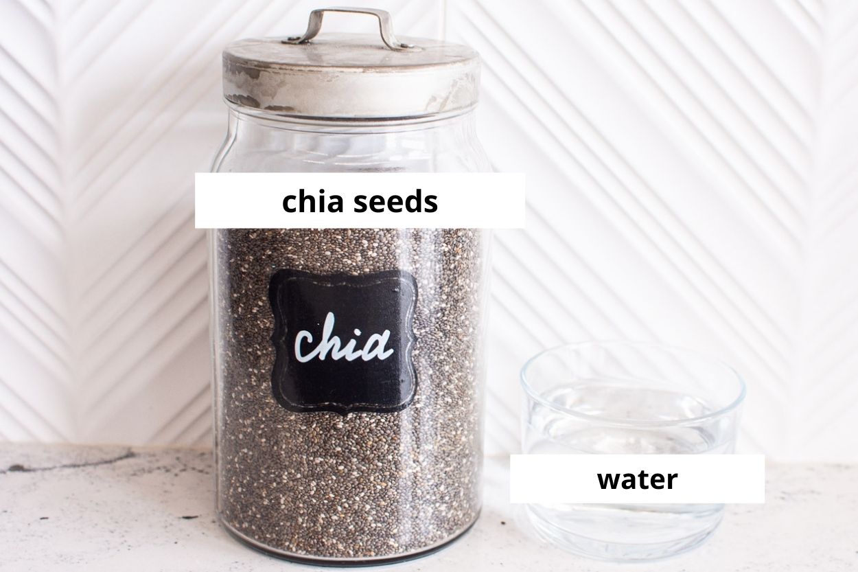 Chia seeds in glass jar and water in a glass on a counter.