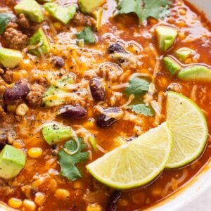Turkey taco soup with cheese, avocado, cilantro and lime served in a bowl.