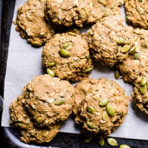 Healthy pumpkin cookies on a baking sheet with pumpkin seeds around.