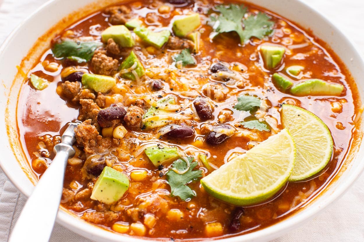 Turkey taco soup garnished with lime, avocado and cilantro served in a bowl with spoon.