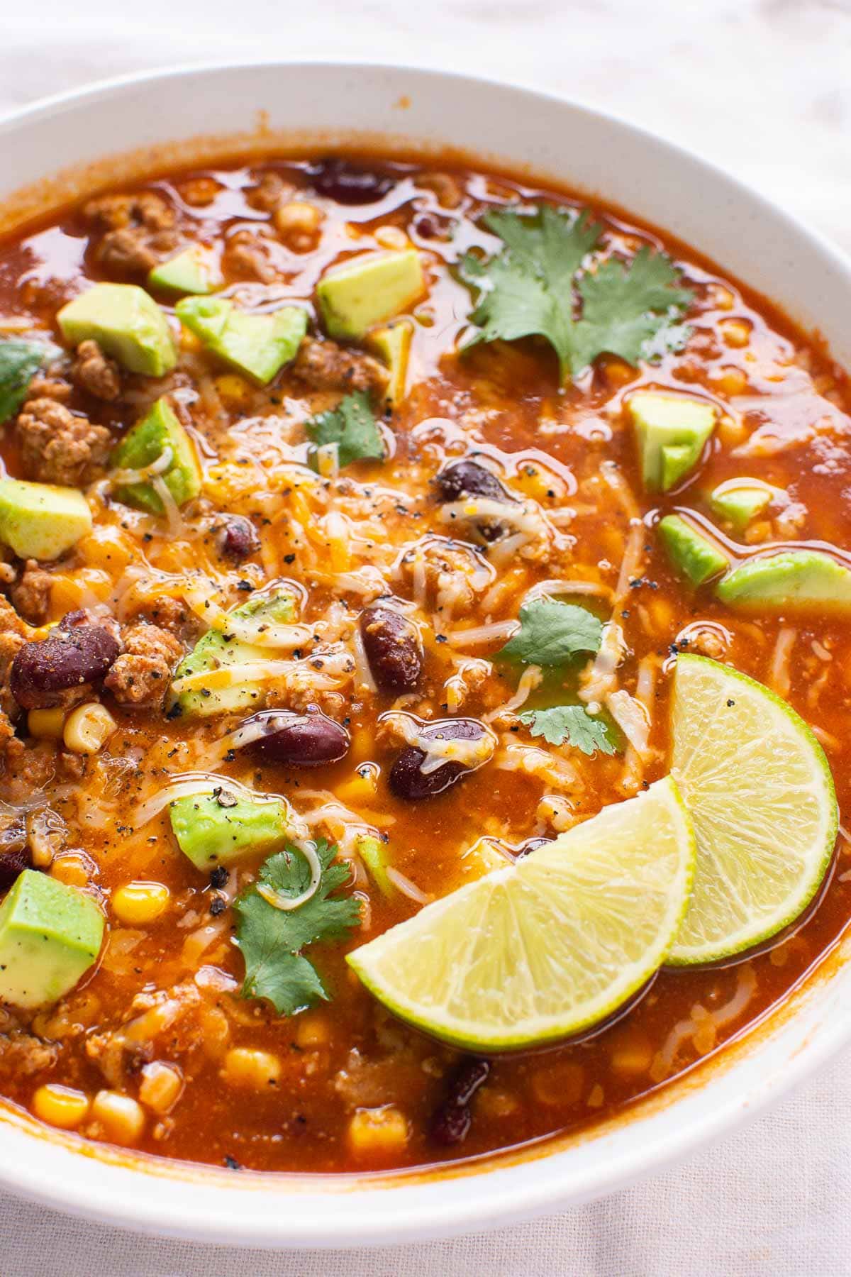 Turkey taco soup garnished with avocado, cheese, cilantro and lime served in a bowl.