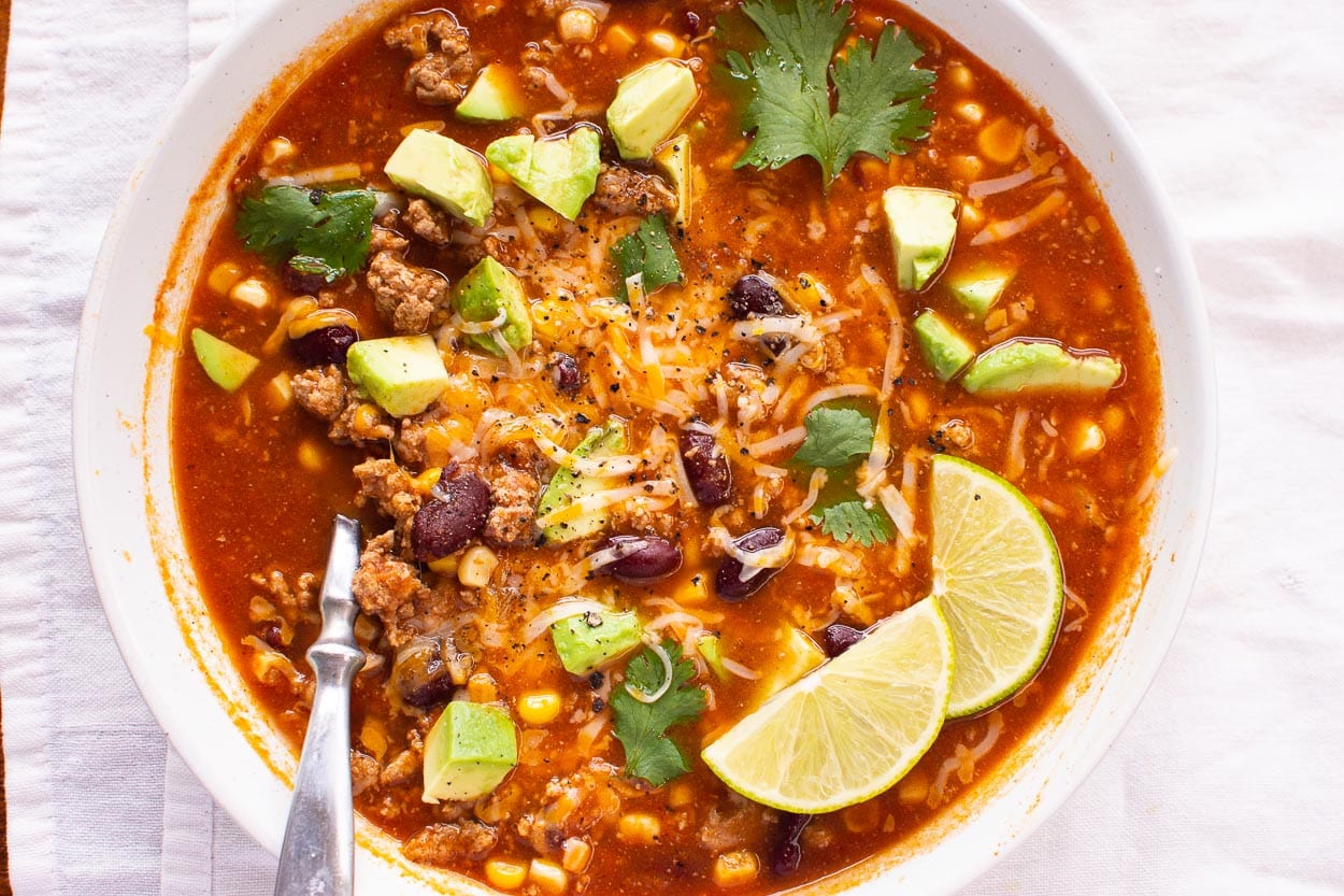 Turkey taco soup in a bowl garnished with lime, cheese, avocado and cilantro.
