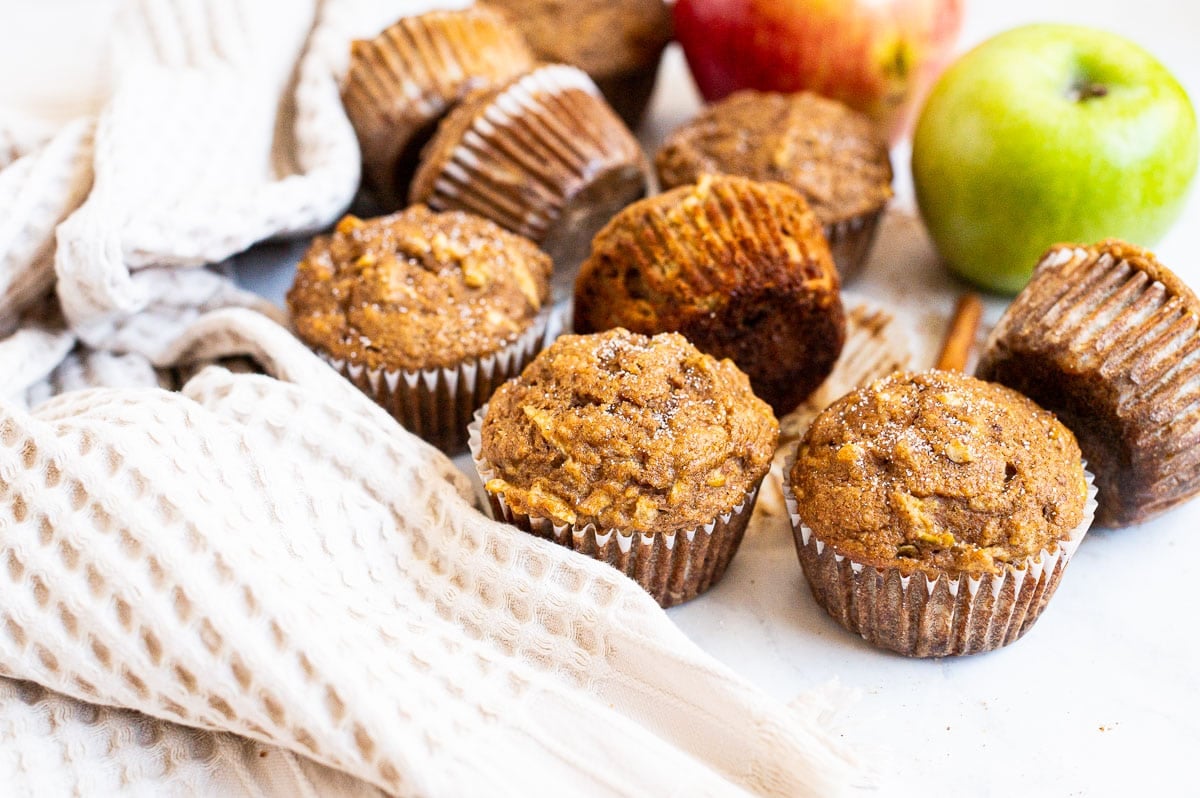 Apple muffins, apples and towel on a counter.