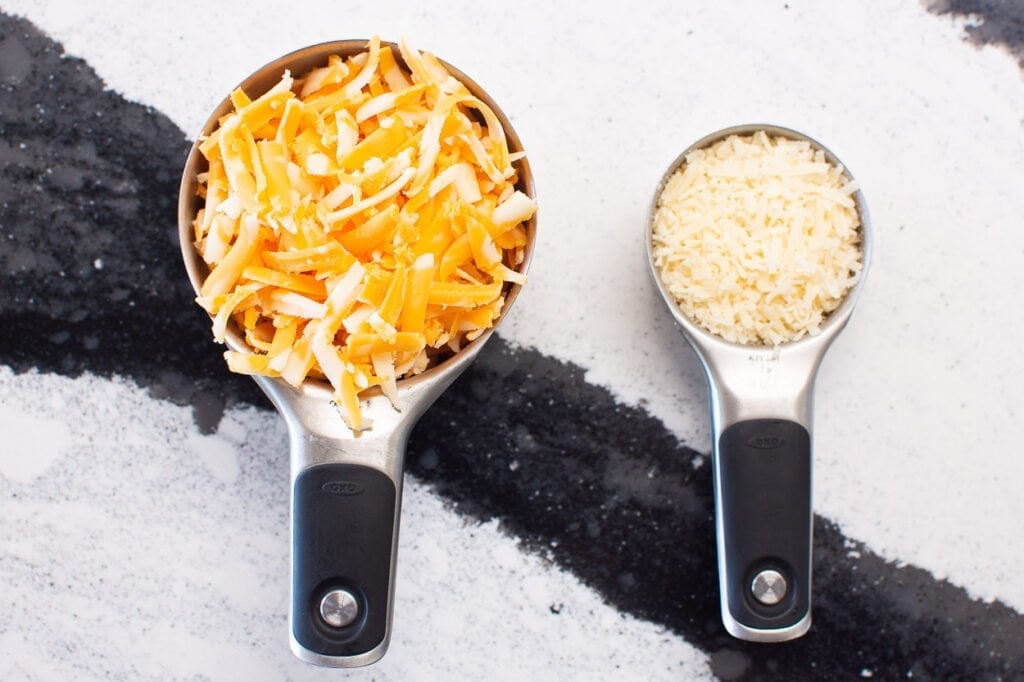 Grated parmesan and cheddar cheese measured for recipe in 2 measuring cups.