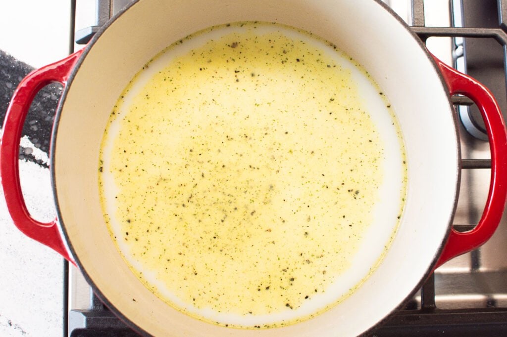 adding broth milk salt pepper and butter to pot on stove for mac and cheese