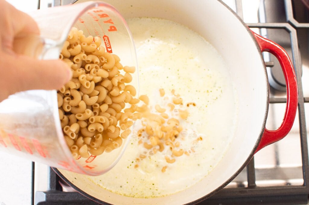 Adding elbow macaroni to liquid ingredients on stove.